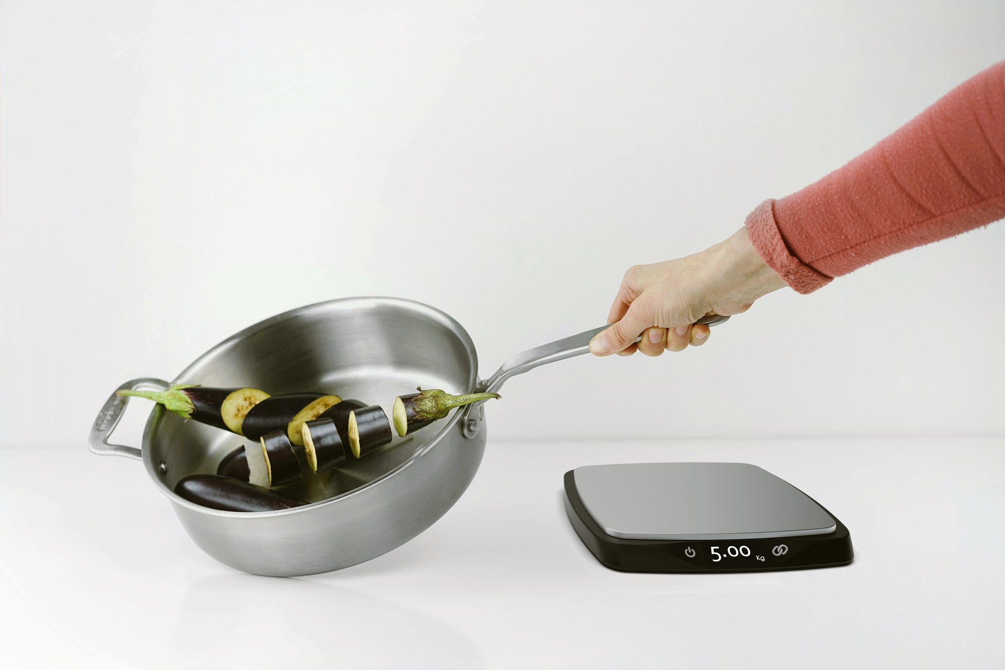 Pluto in use - a hand tips chopped vegetables from a pan beside the scale reading 5.00 kg