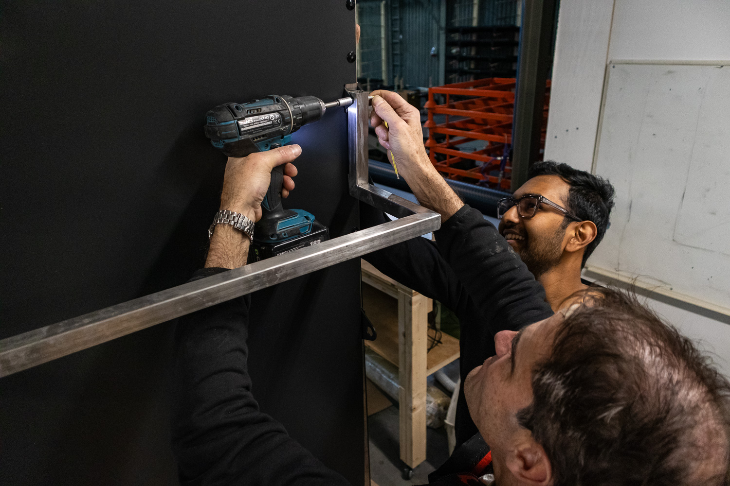 Two people fixing the metal back-box together with a drill